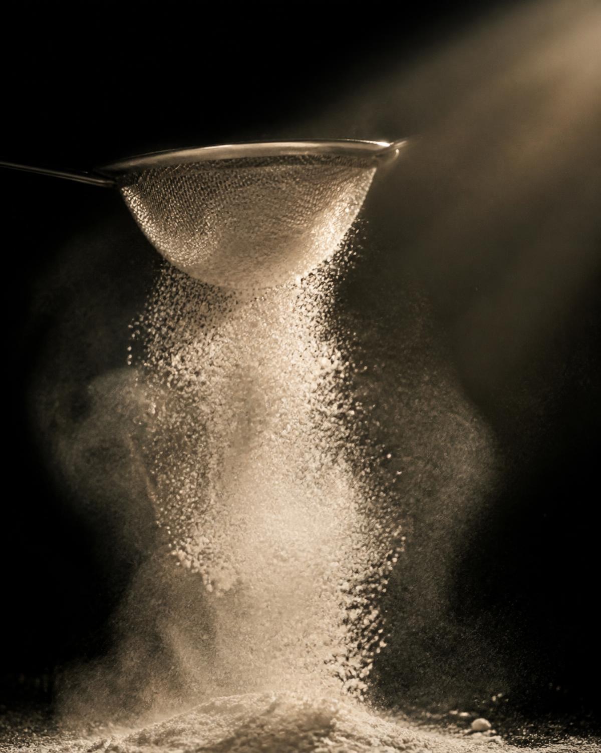 Farine tamisée dans un rai de lumière au fournil